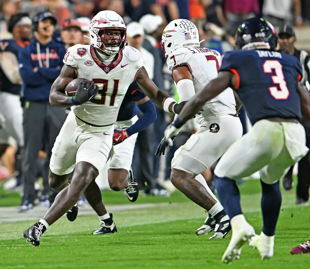 Florida State freshman wide receiver Elijah Moore (#81) in white uniform runs with football after making a catch, evading defenders on the field