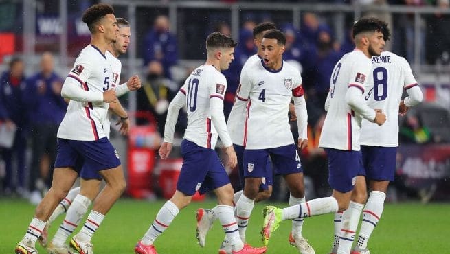 USMNT players in white jerseys celebrate together after scoring goal against Mexico in World Cup qualifier