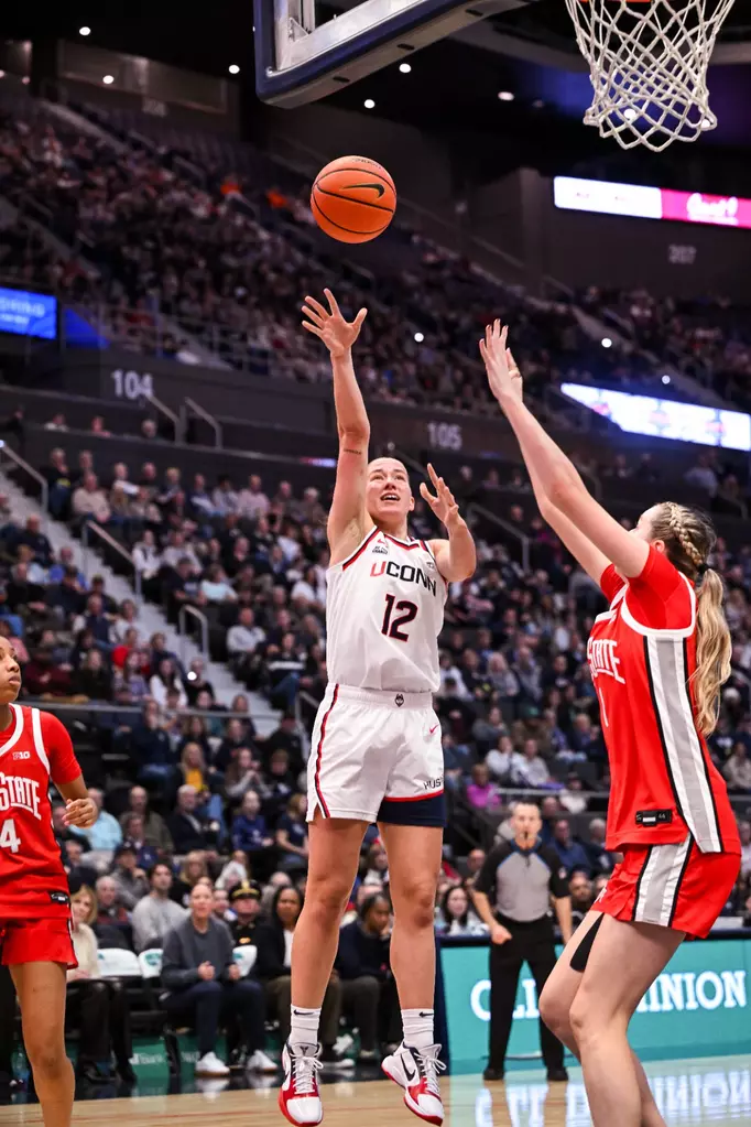 Ashlynn Shade #12 of the UConn Huskies drives against an Ohio State Buckeyes defender during their game at PeoplesBank Arena in Hartford, Connecticut on November 16, 2025.