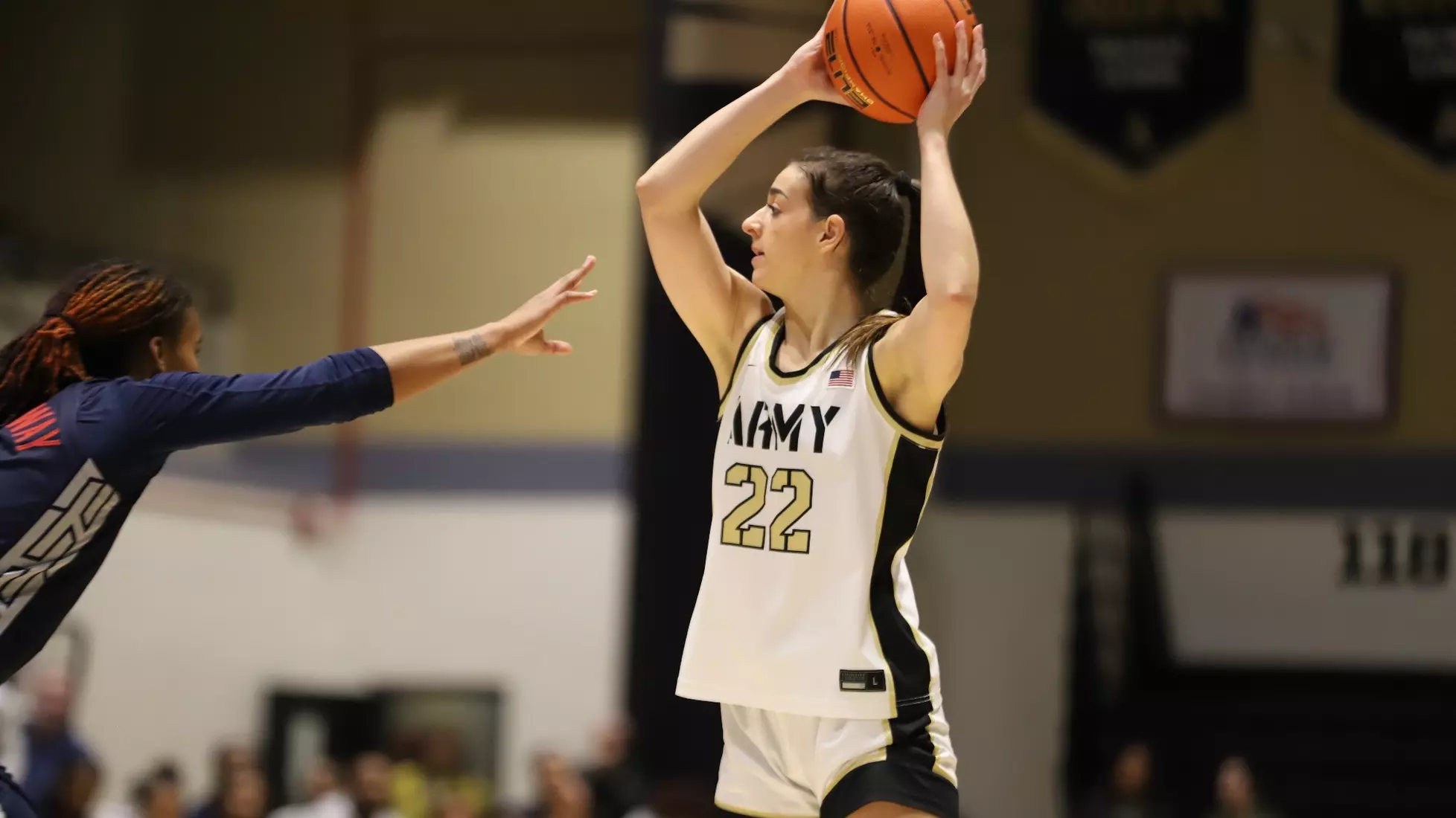 Taylor Wilson (#22) of the Army Black Knights women’s basketball team holds the ball overhead, looking to pass as a defender closes in during a game.