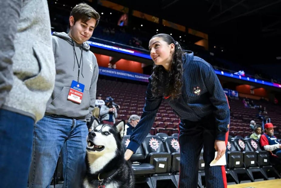 Morgan Cheli of UConn greets the UConn Husky mascot pre‑game, sharing a focused but light moment courtside before tipoff.