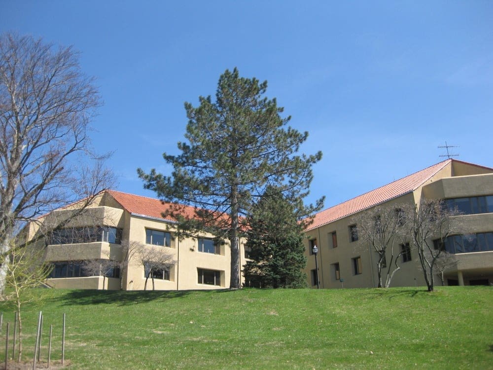 Rosary Hill Home facility in Hawthorne, NY with two beige buildings and a large evergreen tree.