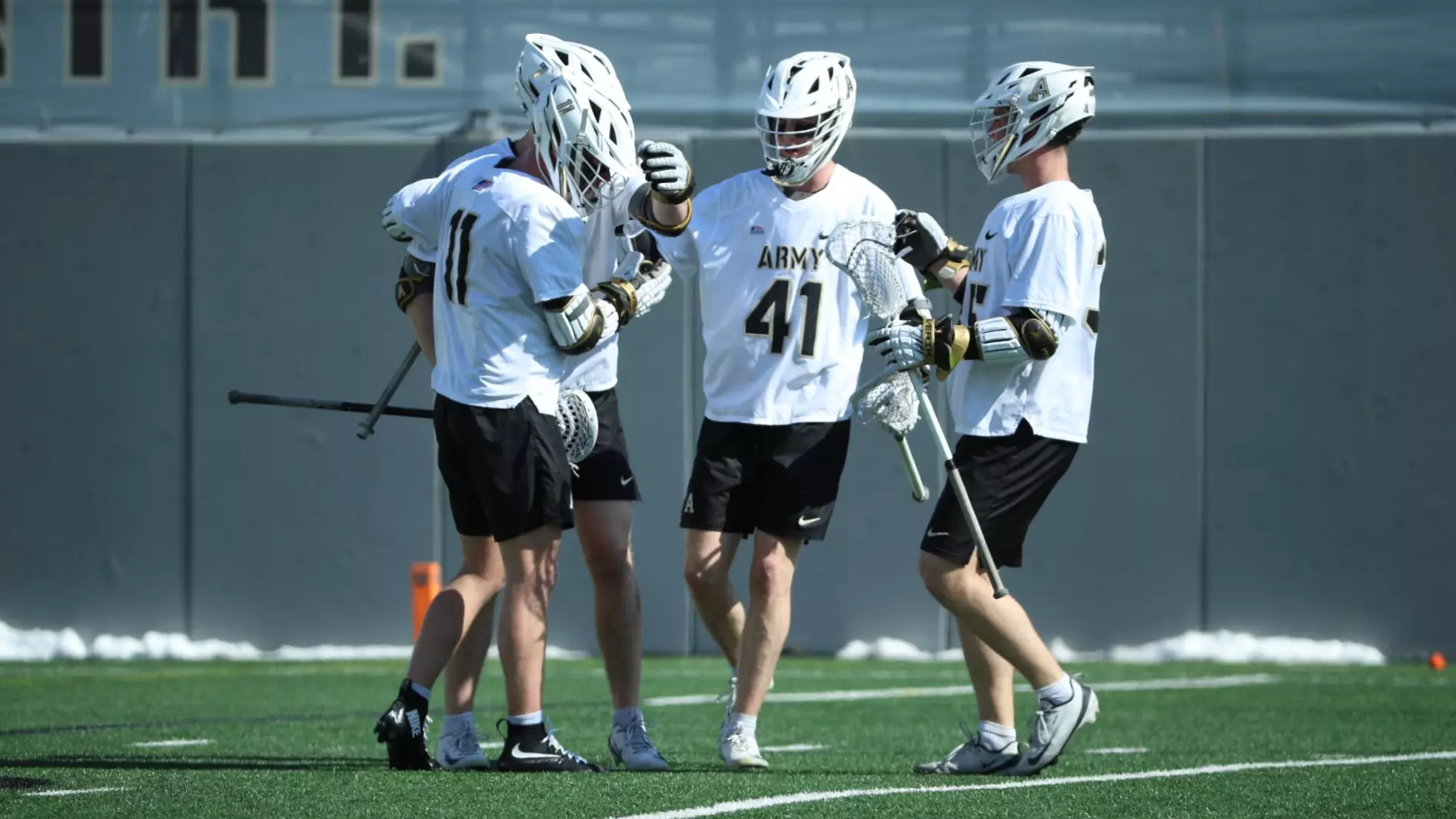Army men’s lacrosse players gather in a tight on‑field huddle celebrating during a game at Michie Stadium.